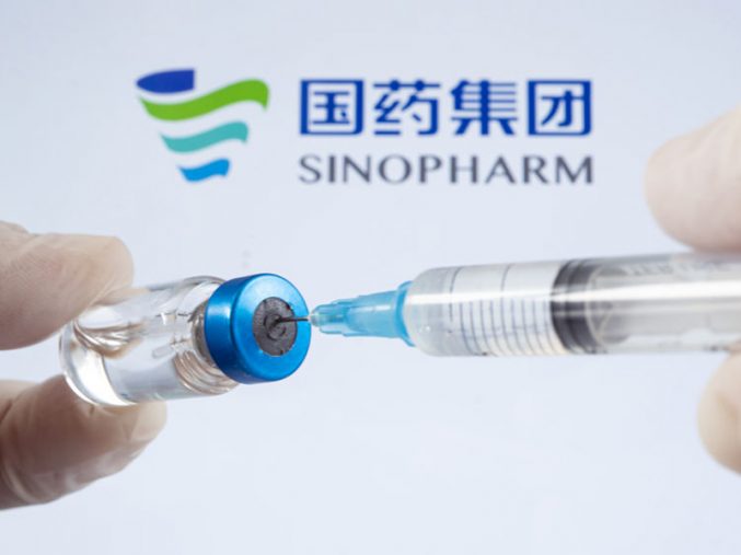 A vaccination syringe and a glass ampoule with a clear liquid on a blue background with the logo of Sinopharm pharmaceutical company. March 13, Barnaul, Russia.