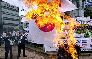 South Korean civic group members burn a Japanese national flag during an anti-Japan rally at the Japanese consulate in Pusan, 400 km (248 miles) southeast of Seoul, South korea, Thursday, July 12, 2001. They protested against Japan's refusal to revise controversial history textbooks accused of glossing over Japan's wartime atrocities. (AP Photo/ Yonhap) **KOREA OUT**